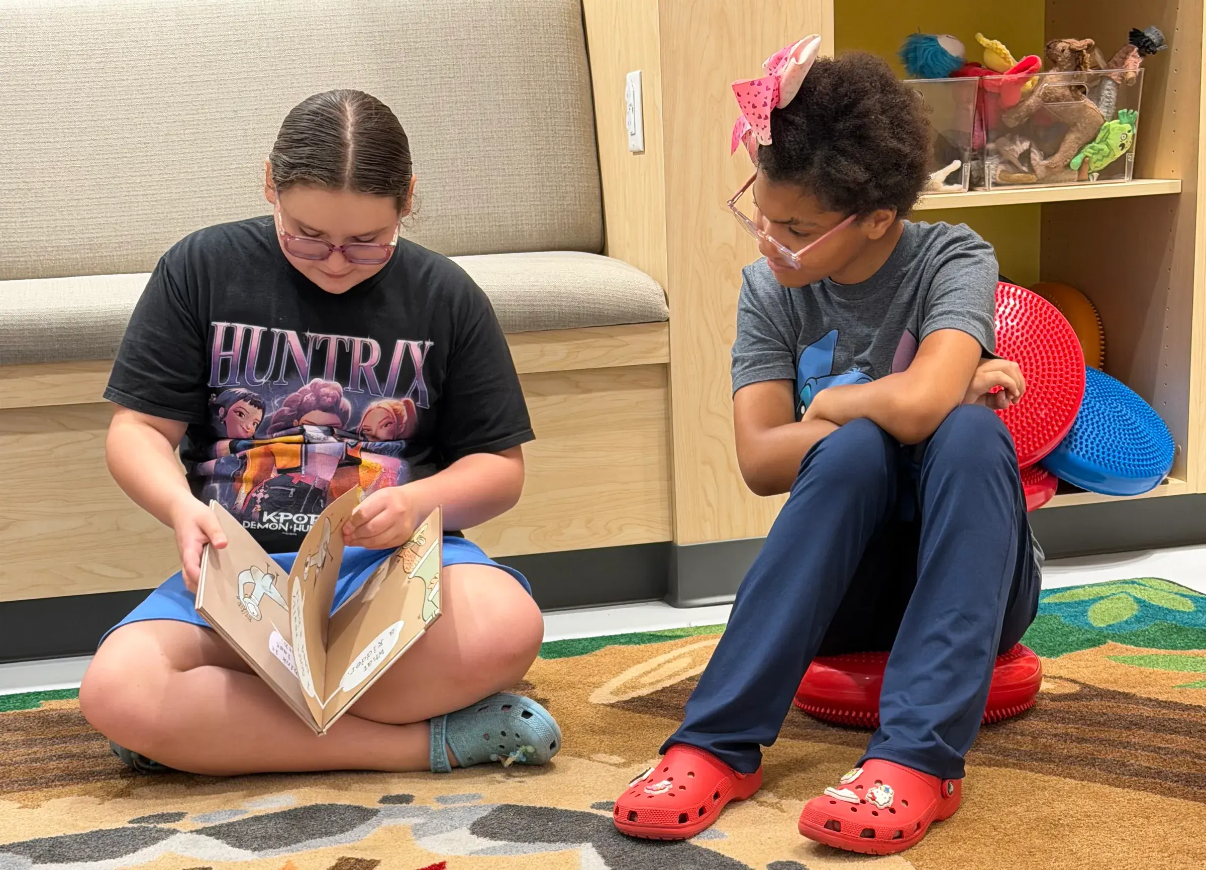 Two young people look at a book together in a calm play space.