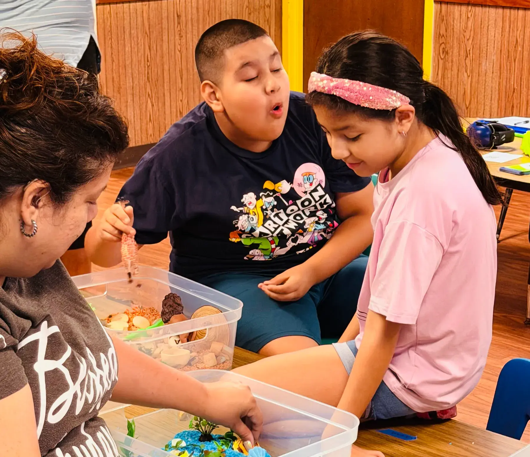 Three people gathered around sensory exploration trays during a hands-on activity.