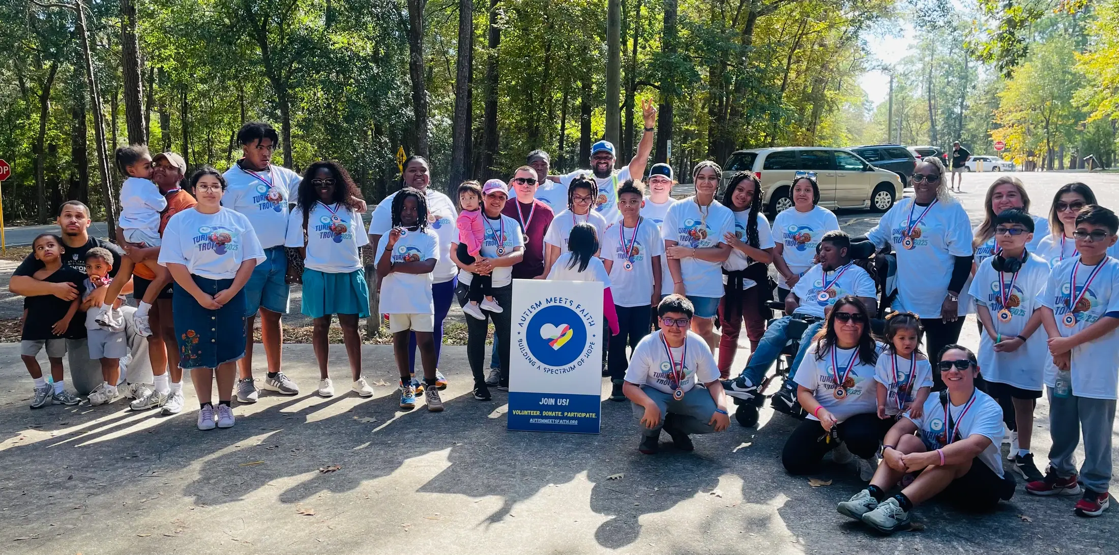 Autism Meets Faith participants and families gather outdoors in Turkey Trot shirts and medals.
